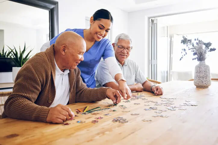 A caregiver and senior men doing a puzzle together, highlighting great assisted living care at The Gables Assisted Living at Spring Lake