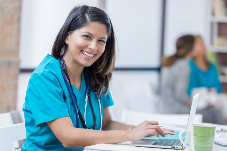 A smiling nurse working on her laptop in a bright, modern healthcare setting in Shreveport, LA