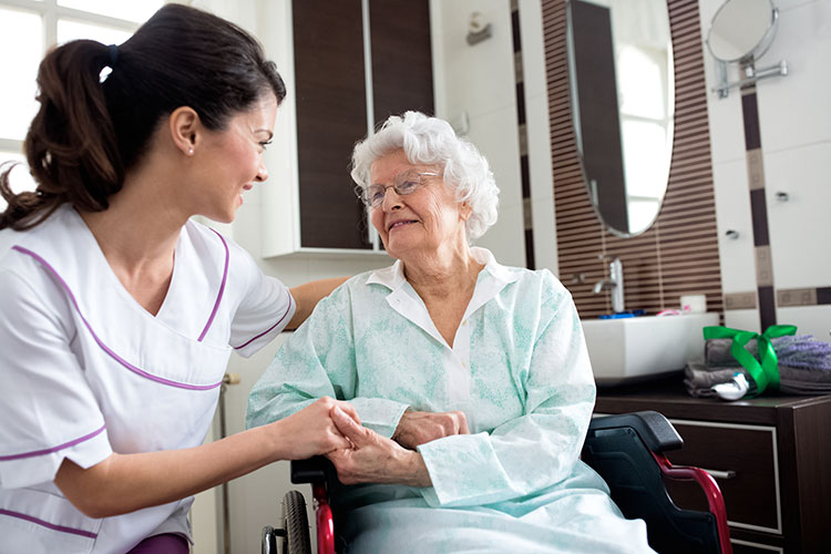 A memory care CNA holds hands with an elderly lady in a wheelchair in Shreveport, LA