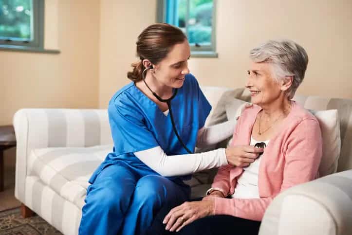 Caregiver using stethoscope to take senior womans heart rate
