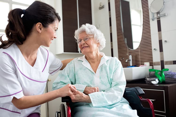 Memory care cna holds hands with elderly lady in wheelchair